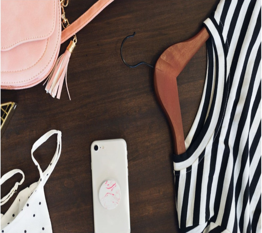 Striped top, phone, pink bag, and hanger on a wooden surface