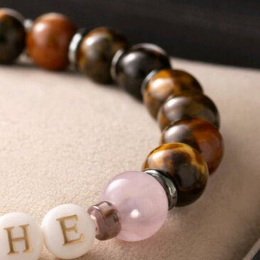 A close up of a beaded bracelet showing the letters H E, on a white background.