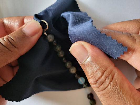 A man cleaning sterling silver semi precious beaded jewellery with a blue cloth.