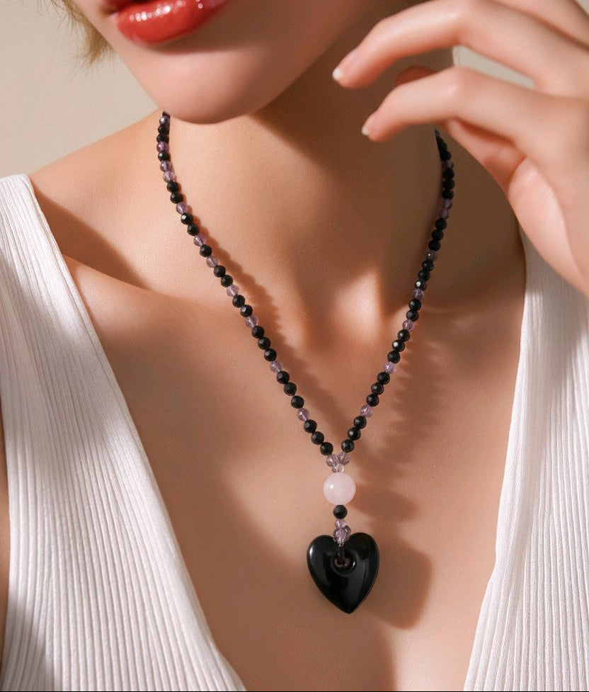 Woman wearing a necklace with a large heart and pink, black and purple stones.