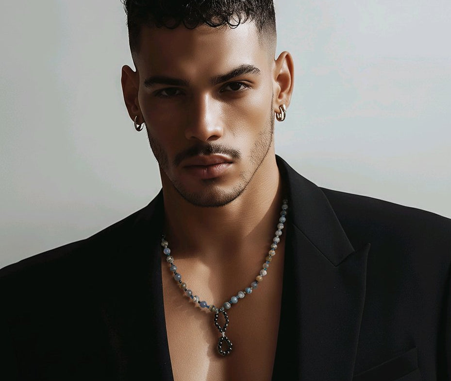 Man wearing a necklace, with a black jacket and a greyish background.