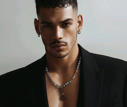 Man wearing a necklace, with a black jacket and a greyish background.