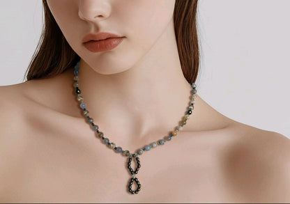 A woman standing with a greyish background wearing a necklace.