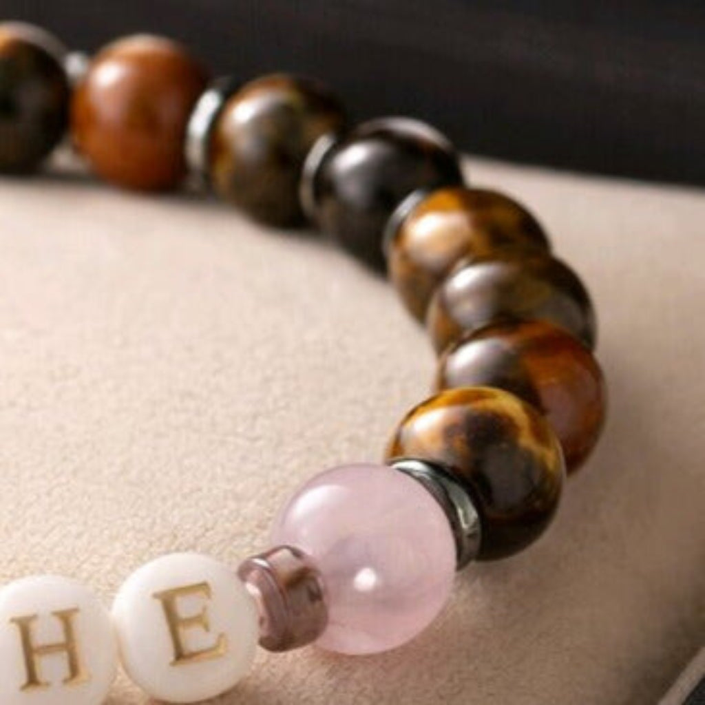 A close up of a beaded bracelet showing the letters H E, on a white background.