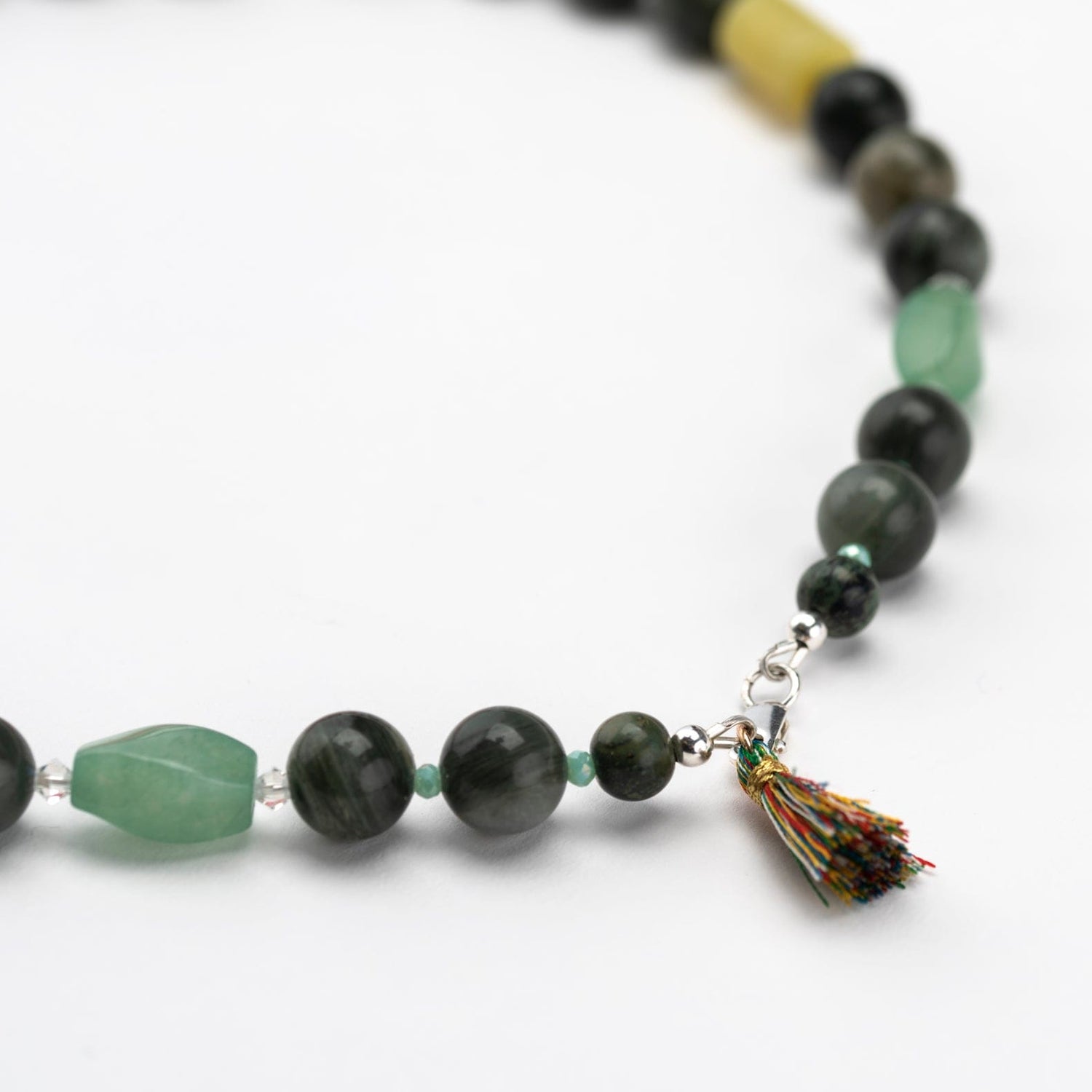 Various green colour beads with a multioloured tassel on a white background.