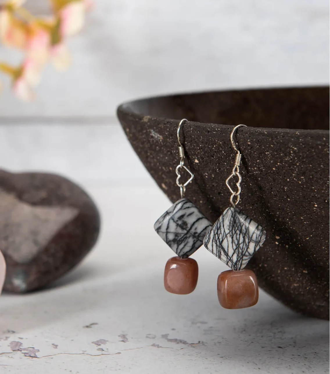 Earrings hanging on the edge of a brown bowl.